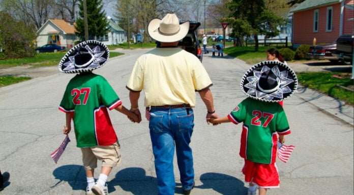 A family celebrates Cinco de Mayo in Port Huron, Michigan. A man in a cowboy hat holds the hands of two young boys in mariachi sombreros, holding US flags